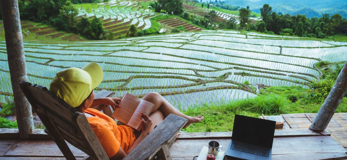 Asian woman travel nature. Travel relax. sit reading book the balcony of the resort. View of the field on the Moutain in summer. Thailand