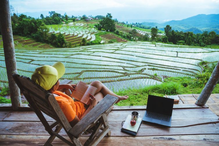 Asian woman travel nature. Travel relax. sit reading book the balcony of the resort. View of the field on the Moutain in summer. Thailand