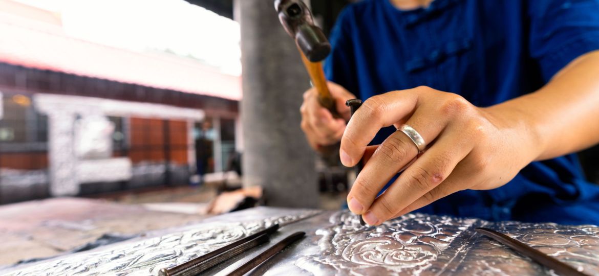 Hand of a woman cutting silverware. Thai craftman are making silverware. A craftsman carves intricate drawings into silver or aluminium which is used for silverware.