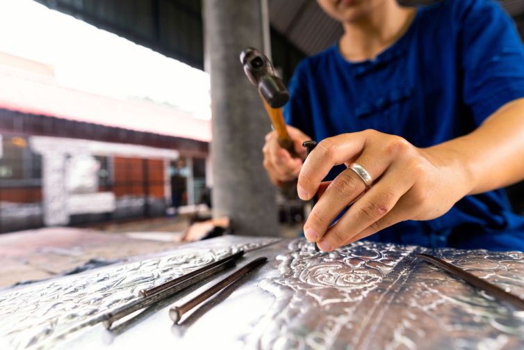 Hand of a woman cutting silverware. Thai craftman are making silverware. A craftsman carves intricate drawings into silver or aluminium which is used for silverware.