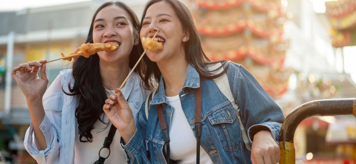 Two beautiful Asian female tourists are enjoy street food in Thailand while exploring the city.